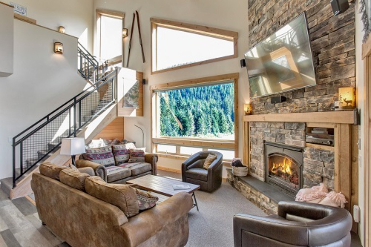 Powder Lodging Vacation Rental Interior - living room with large stone fireplace and views of the forest