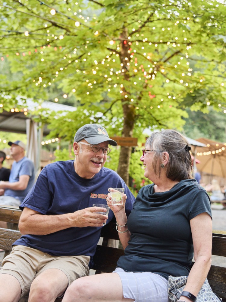 Two people hold drinks and look at each other while in conversation on a bench