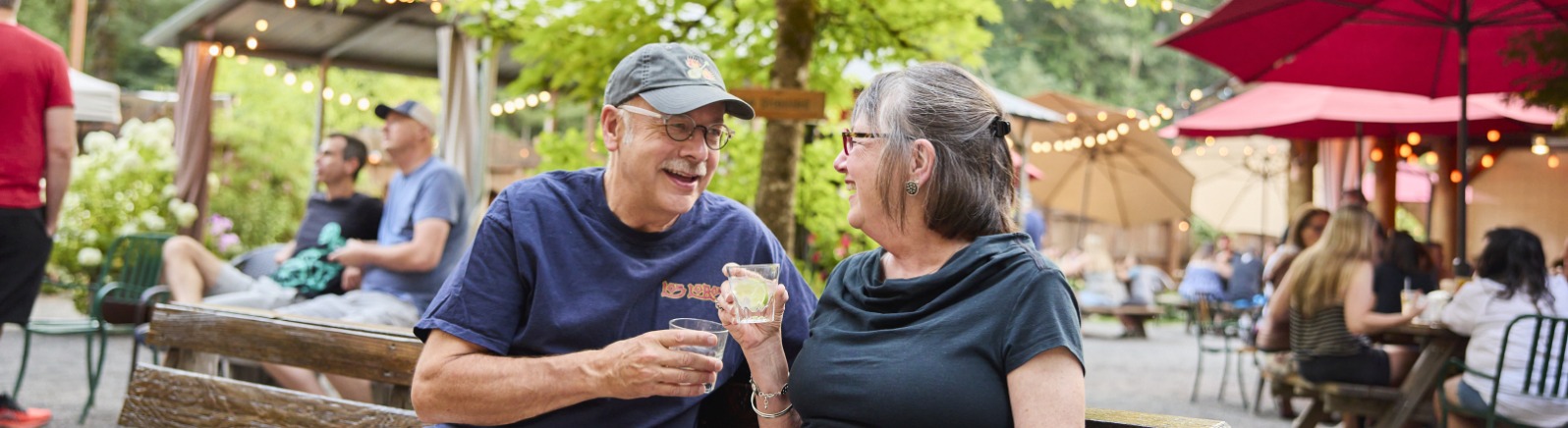 Two people hold drinks and look at each other while in conversation on a bench