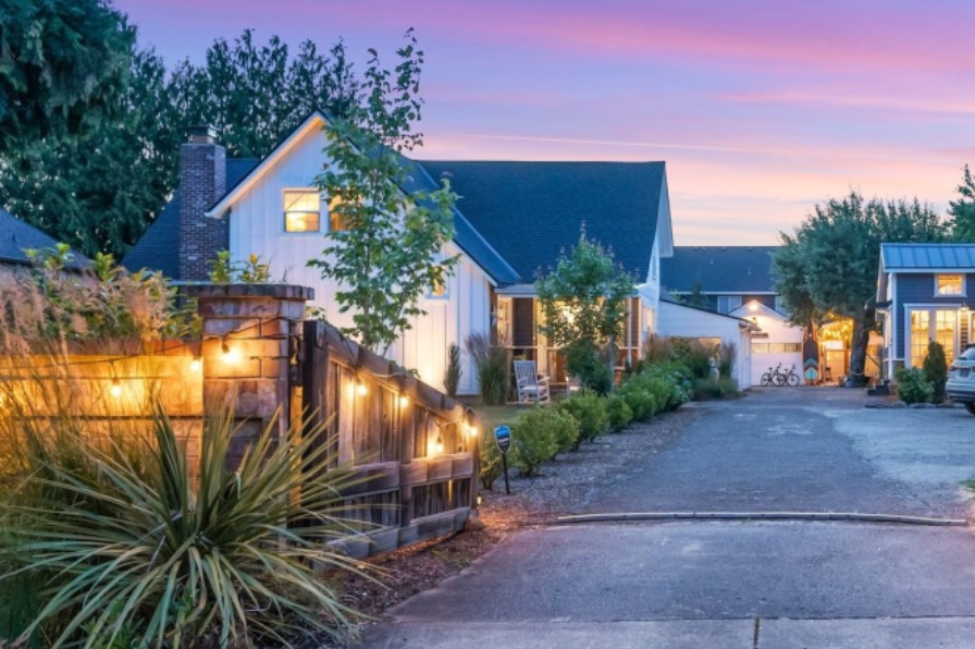 driveway entrance to Our Sweet Retreat vacation rental at dusk. The landscaping is lit with garden lights and we see a house and ADU in the distance