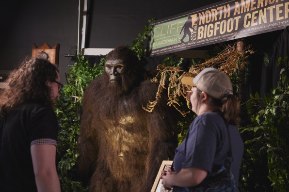Two visitors to a museum look at a large brown furry Bigfoot model.
