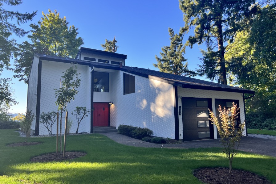 Exterior of the tall, white, Forest View Ridge Vacation rental. Black trim with a red front door and tall vaulted roof and windows. grass and trees out front