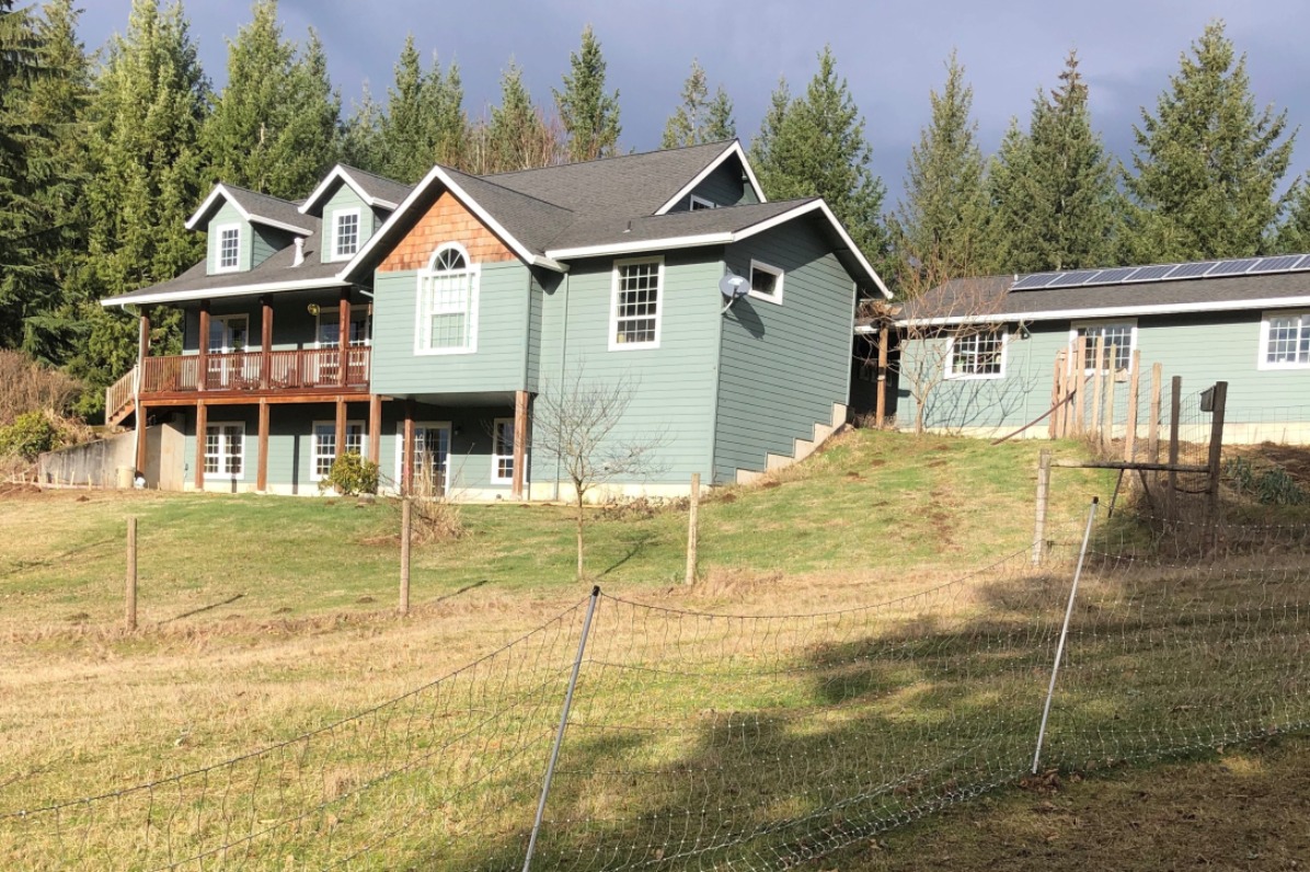 Chickens peck the ground outside a green farm home. 