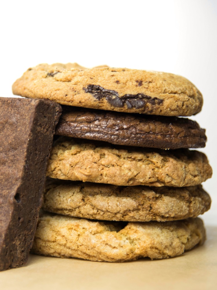 A single brownie leans against a stack of five cookies