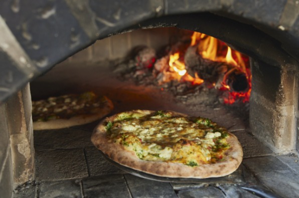 A pizza slides out of a brick, woodfired pizza oven at Our Table Cooperative 