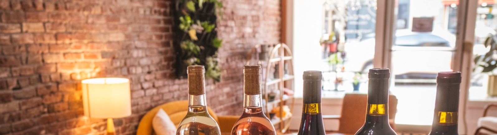 Five bottles of Corcilla Cellars Wines sit on a table with trays of cookies. A half full glass of red wine sits in the foreground. 