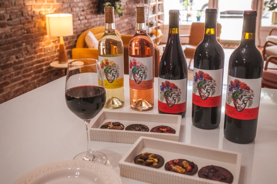 Five bottles of Corcilla Cellars Wines sit on a table with trays of cookies. A half full glass of red wine sits in the foreground. 