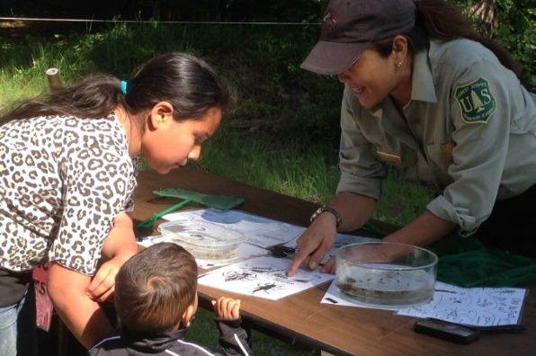 Forest Service fish biologist assisting two children with a learning activity during a Hood River Ranger District fishing clinic.
