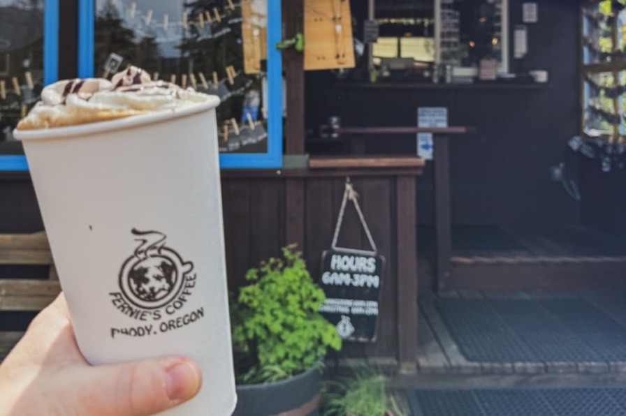 A coffee cup held up in front of coffee shop.