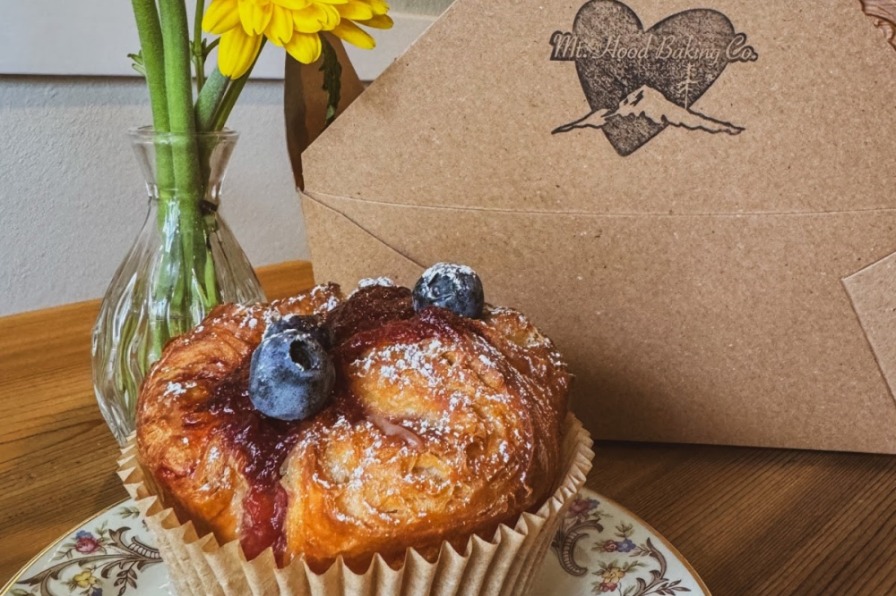 Blueberry muffin with yellow flowers and to-go box on table.