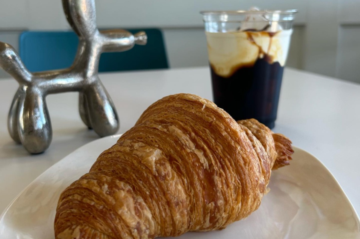 Scone and coffee ice cream drink sit on a white table. Floral print wallpaper in the background