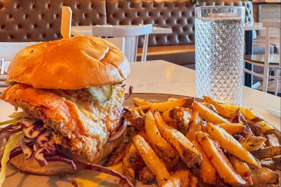 A chicken burger on a bun with a large plate of fries.