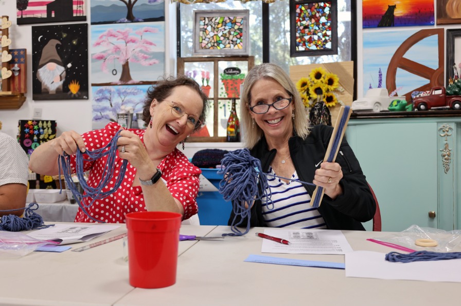 Two people hold up yarn and smile for the camera at an art class