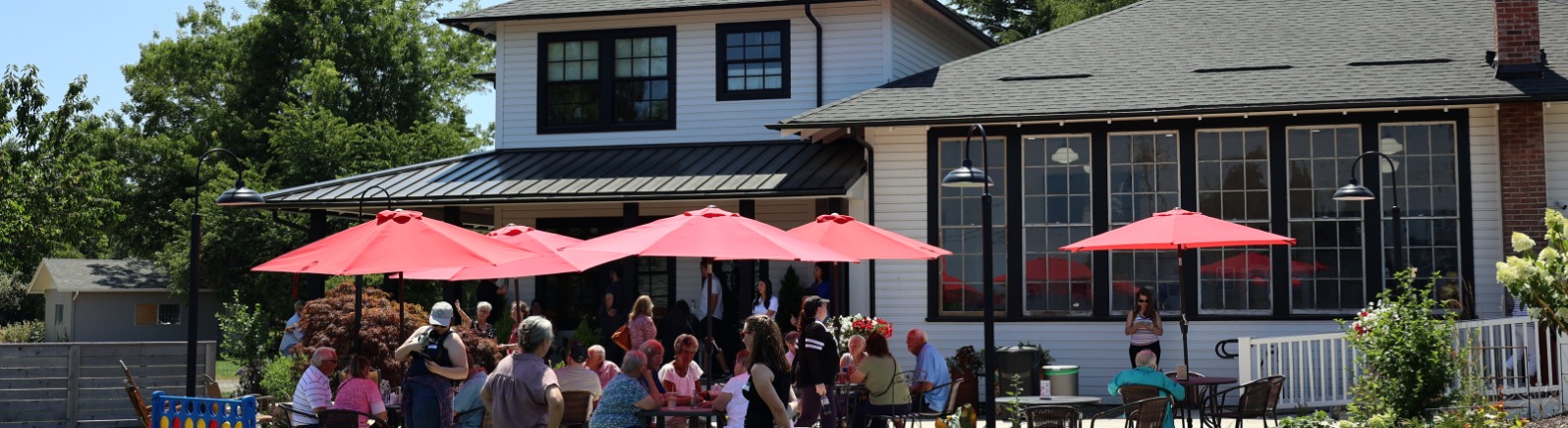 A crowd of people sit at tables under red umbrellas on the patio of Whiskey Hill Store