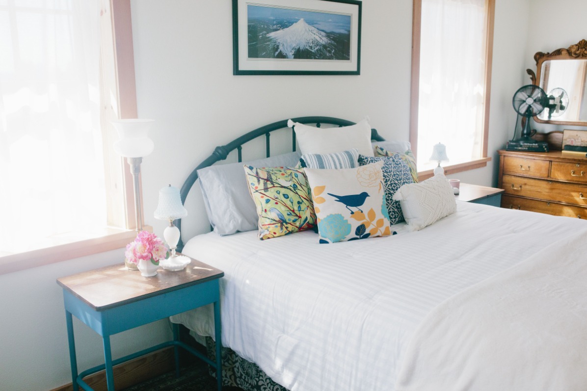 A photo of Mt Hood hangs on the wall above a Queen sized bed with a blue comforter flanked by blue side tables. 
