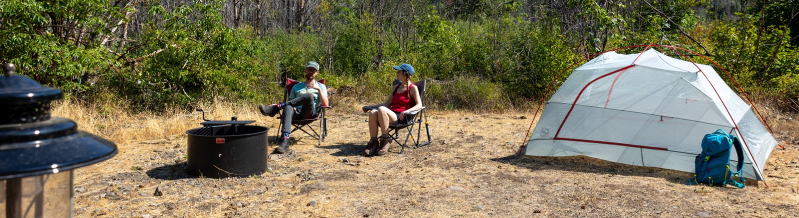 Two campers sit near a fire ring and a tent