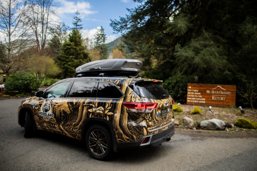 Hoodland Shuttle car in front of the Mt Hood Oregon Resort Entrance. Car is wrapped in illustrations of mt hood forest
