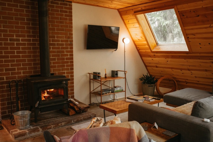 Cozy living space with couches, lamps, a TV, fireplace and a window looking into the forest