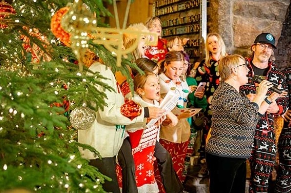 Carolers gather and sing around a decorated tree.