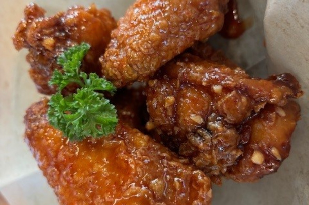 Four pieces of Hearty K-Bop fried chicken sit in a paper-lined basket. 