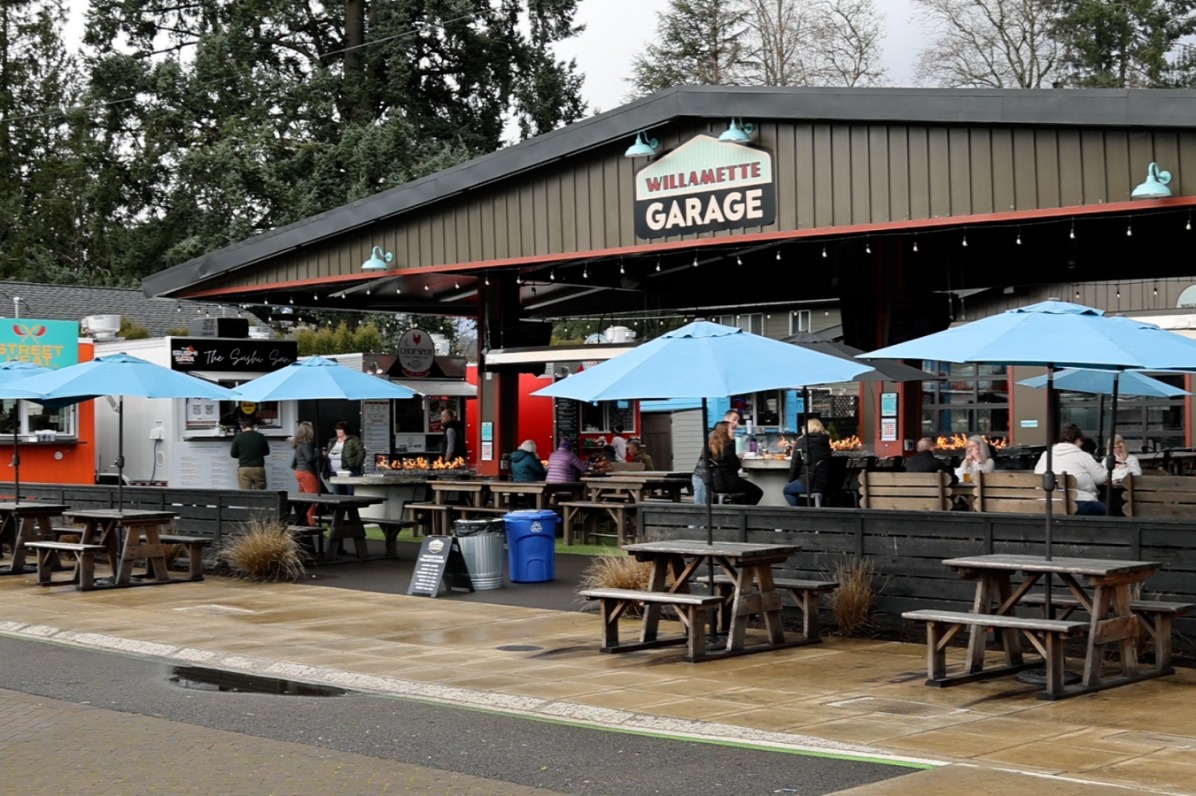 Blue umbrellas cover picnic tables surrounded by food carts.
