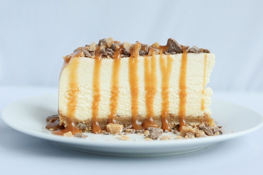 Caramel is drizzled all over the top and sides of a slice of salted caramel cheesecake.
