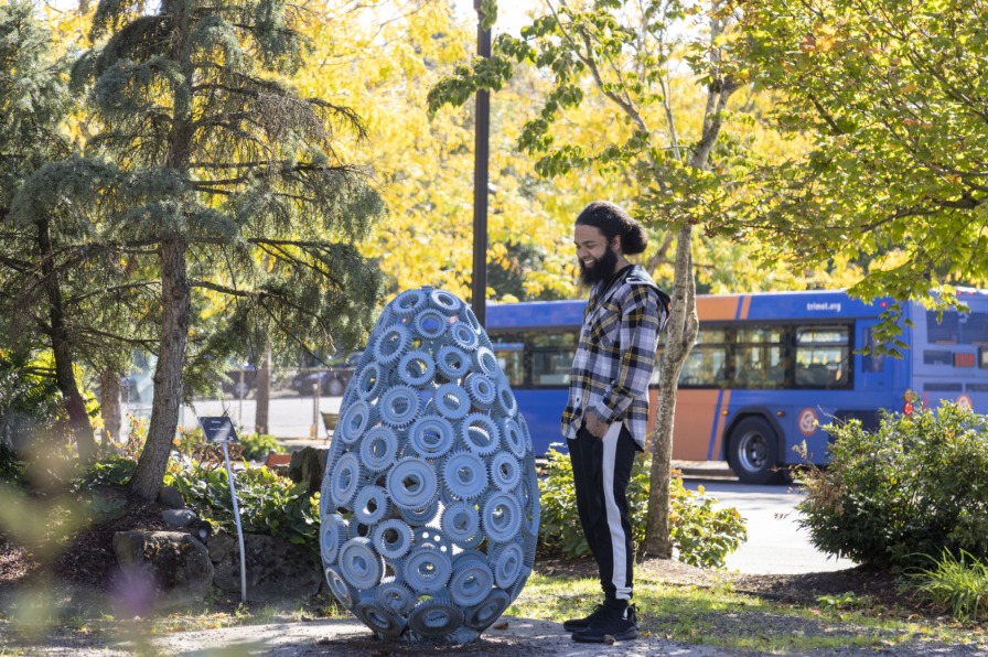 A visitor looks at a giant blue egg in a park filled with green trees.