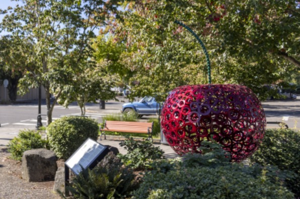 A bright red cherry statue sits in bushes of green