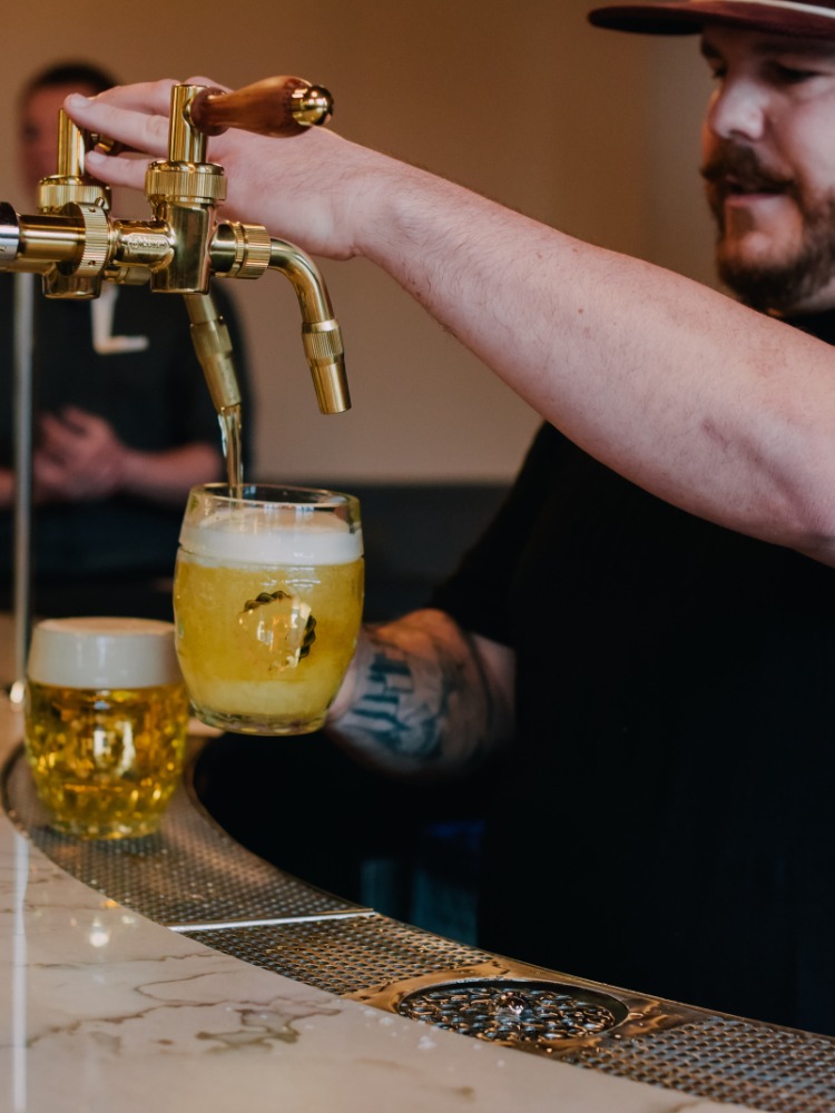 A bar tender fills a beer glass with golden beverage