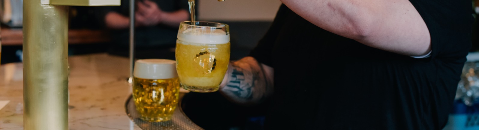 A bar tender fills a beer glass with golden beverage