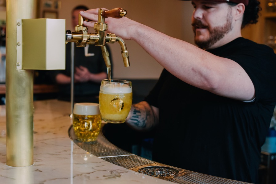 A bar tender fills a beer glass with golden beverage