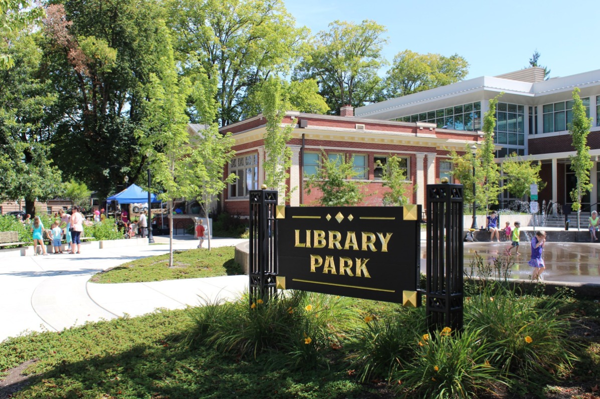 A brick building next to a splash pad outside a sign.