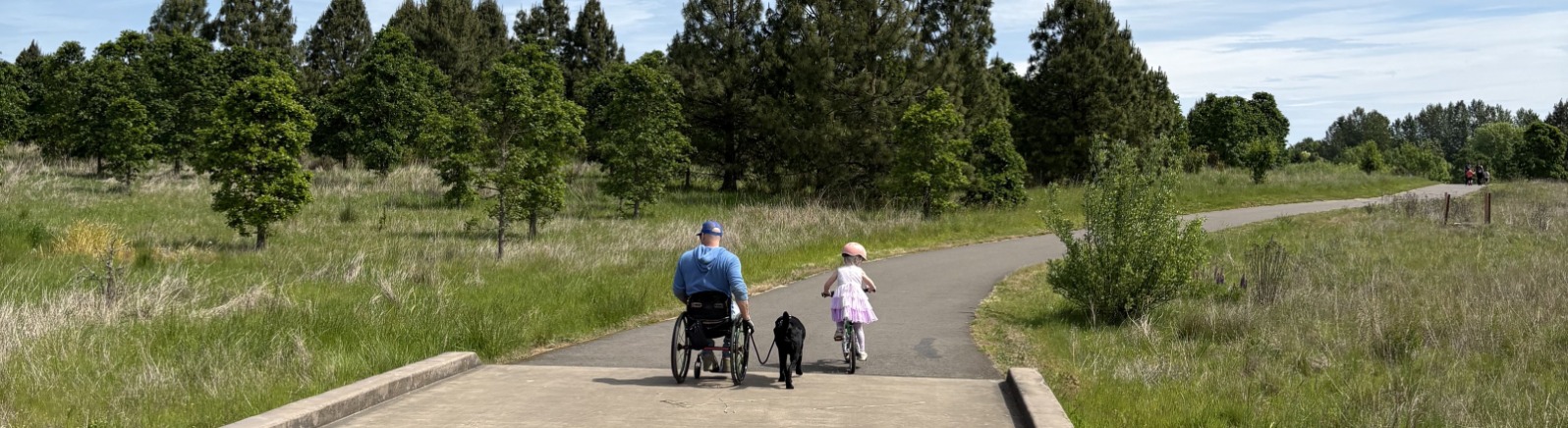 A person in a wheel chair on a cement trail next to a child on a bike.
