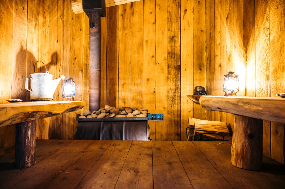 Inside of a sauna with wood walls and two wood benches and glowing lanterns.