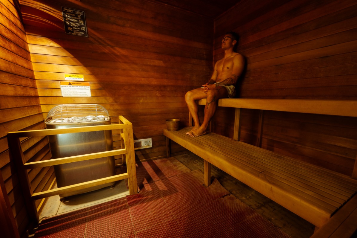 A visitor in a brown wood sauna with two benches.