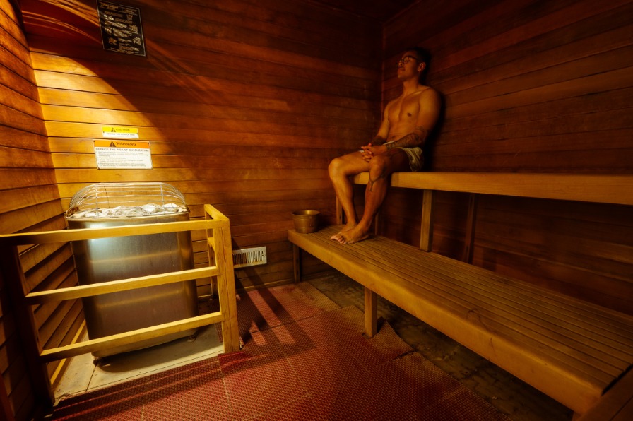 A visitor in a brown wood sauna with two benches.