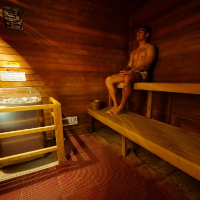 A visitor in a brown wood sauna with two benches.