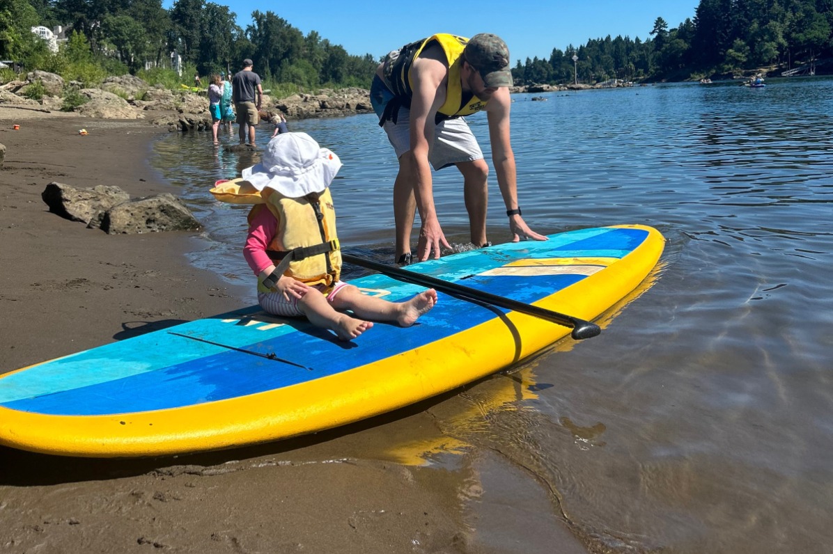 Parent puts child on standup paddleboard in river