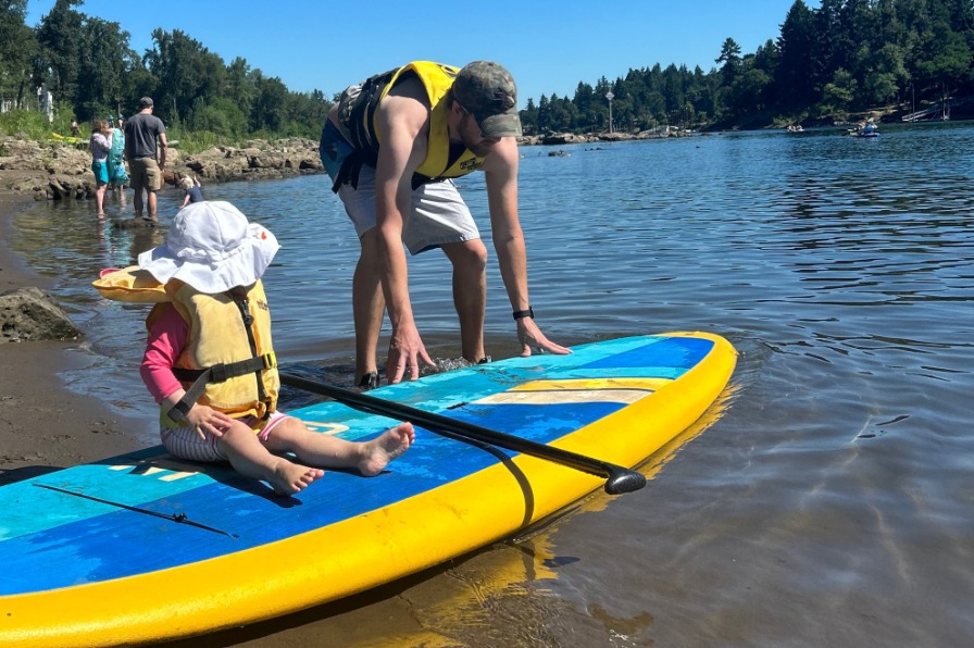 Parent puts child on standup paddleboard in river