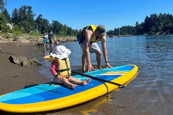 Parent puts child on standup paddleboard in river