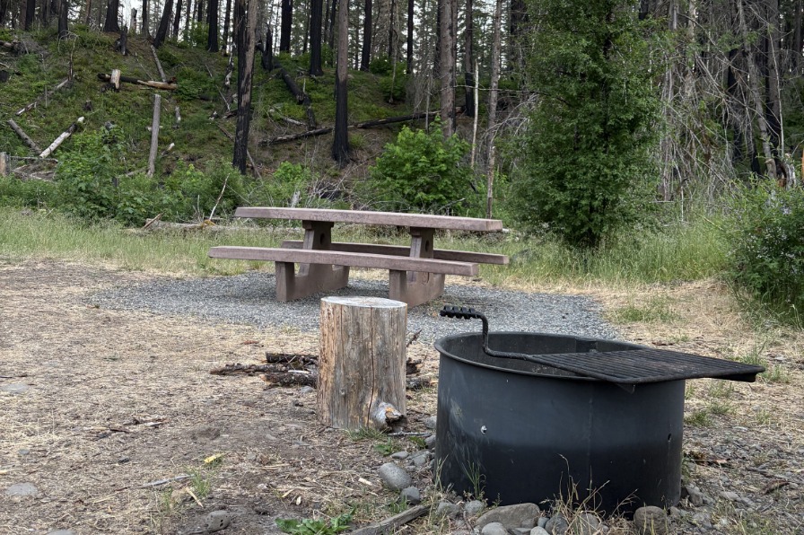 Rainbow Campground A black fire ring sits in front of a brown picnic table