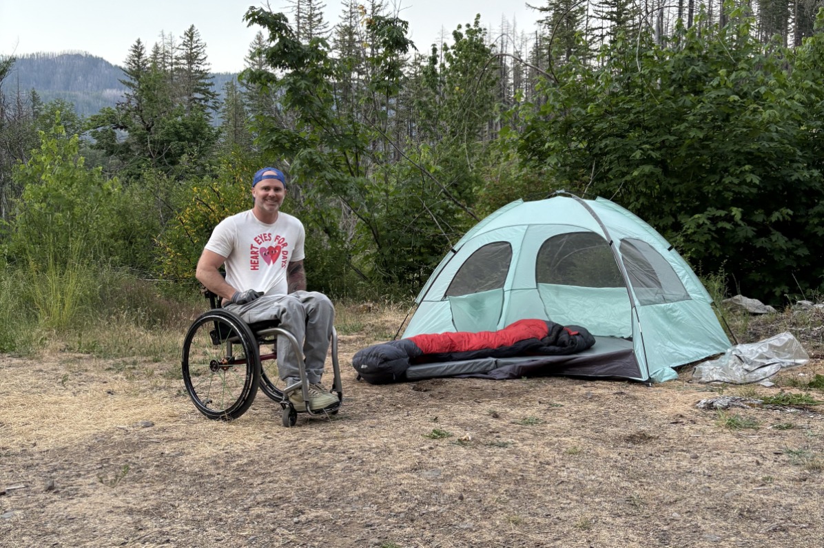 A camper in a wheelchair poses next to a tent.