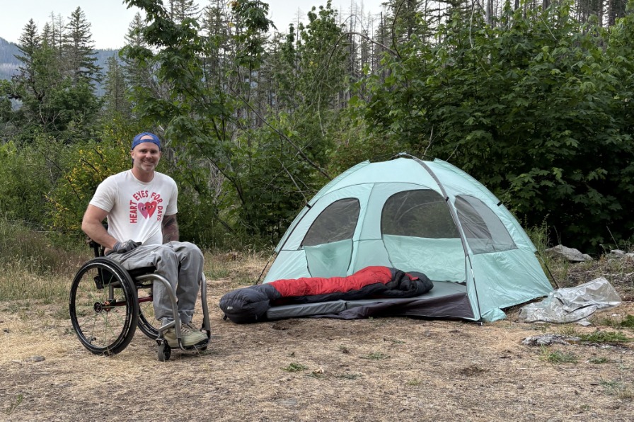 A camper in a wheelchair poses next to a tent.