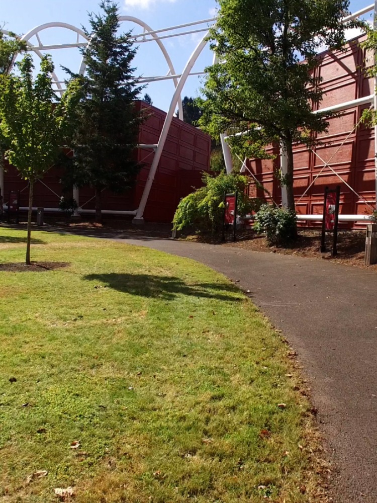 A grey cement path runs along green grass outside of red buildings