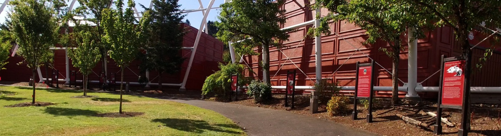 A grey cement path runs along green grass outside of red buildings