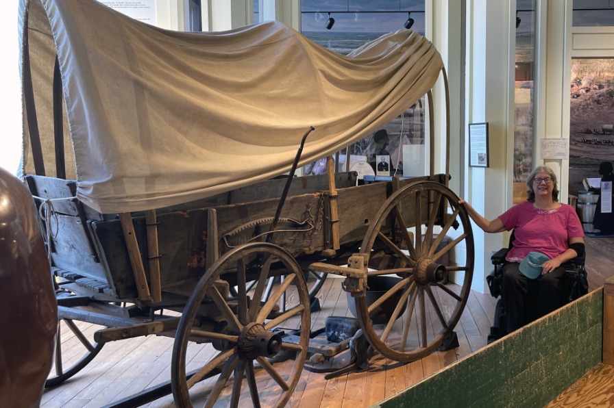 A visitor in a wheelchair poses next to an old wagon in a museum