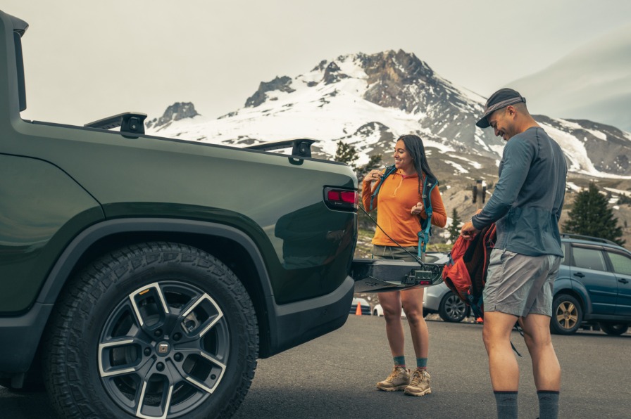 Two people prep their backpacks for a hike on the tailgate of a truck with Mt Hood in the background.