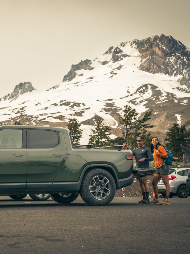 Couple at back of a truck EV charging by Mt. Hood