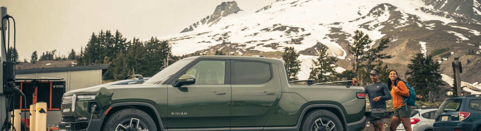 Couple at back of a truck EV charging by Mt. Hood