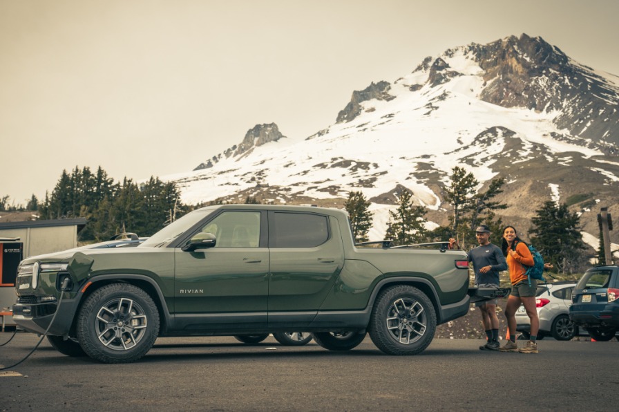 Couple at back of a truck EV charging by Mt. Hood